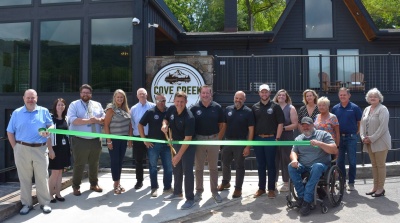 The owners of Cove Creek Lodge and other men and women pose in front of Cove Creek Lodge, Deep Creek Lake, for a ribbon cutting to celebrate its grand opening.
