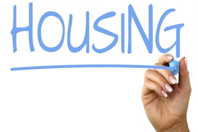 The word "HOUSING" in light blue text, underlined in light blue; a hand holding a light blue pen in the lower righthand corner; all on a white background