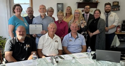 GCCAC CEO Chris Mullet stands with a proclamation celebrating 60 years of the Garrett County Community Action Committee with former and current GCCAC members and Garrett County Commissioners (front) Ryan Savage, Larry Tichnell, and Paul Edwards. 