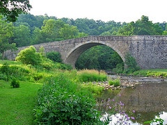 Photo: Historic Casselman River Bridge spanning the Casselman River in Grantsville, Maryland, surrounded by lush green vegetation.