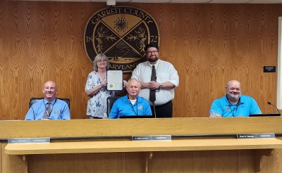 Photo: Seated l-r: Commissioners, Paul Edwards, Larry Tichnell, and Ryan Savage. Standing (l-r): Manager of Business Development Kim Durst and Business Development Specialist Connor Norman. The Garrett County official seal is on the wall in the background.