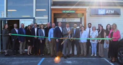 A group of community and business leaders gathers outside Middletown Valley Bank’s Oakland Branch for a ribbon-cutting ceremony, with the group holding a green ribbon in front of the bank entrance.